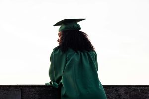 A recent graduate gazes thoughtfully into the distance, wearing a cap and gown, symbolizing reflection on their journey and the future ahead.