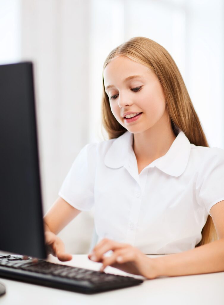 School girl sitting at a desk working on a computer.