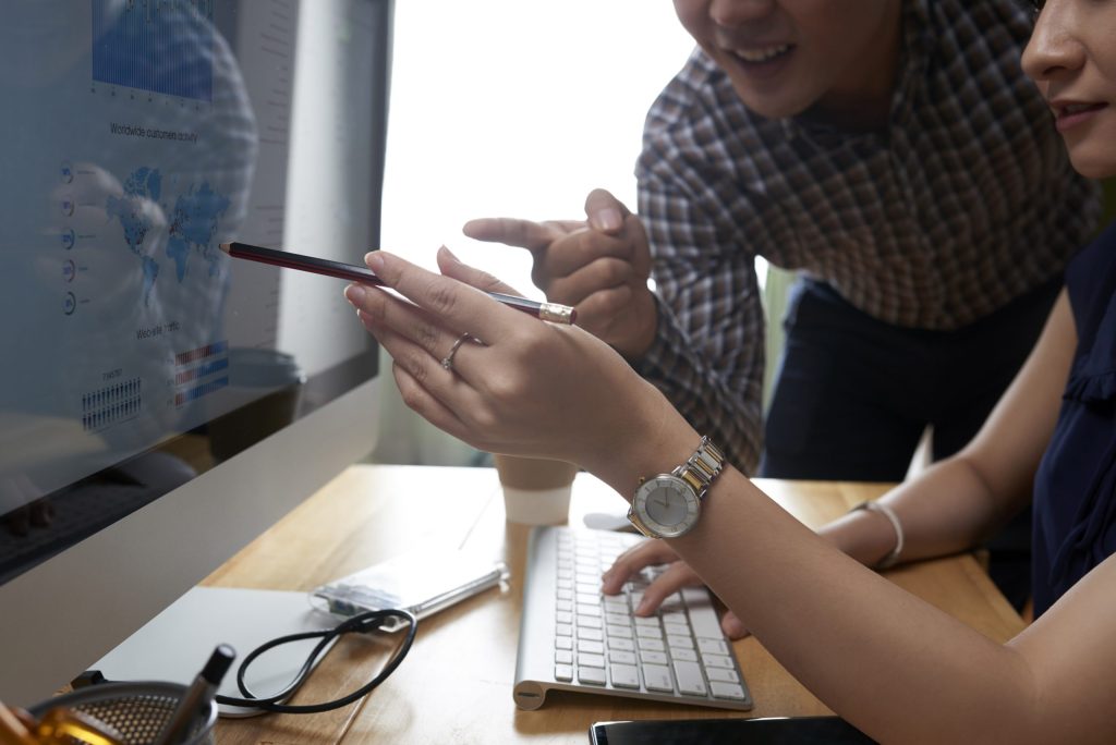Two people sitting at a desk looking at a computer and working.